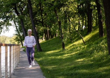 Elderly woman running along a riverside path in a green park, embracing fitness and nature.