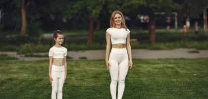 A woman and girl in white activewear standing on a grass field outdoors, smiling.