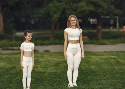 A woman and girl in white activewear standing on a grass field outdoors, smiling.
